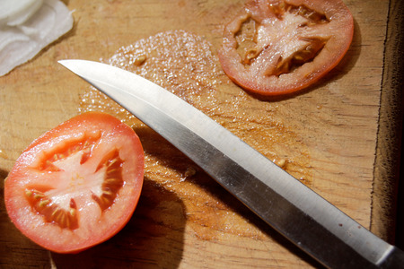 Photograph of a knife, tomato slices and onion on a wood cutting boardの写真素材