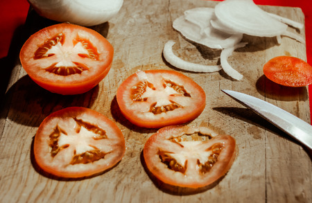 Photograph of a knife, tomato slices and onion on a wood cutting boardの写真素材