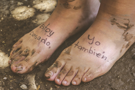 Photograph of a pair of human feet and the phrase in spanish: Estoy cansado, yo tambien, which means: Im tired, me tooの写真素材