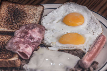 Photograph of a plate with fried eggs, ham, sausage and beansの写真素材
