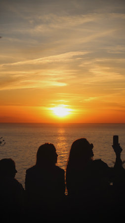 Silhouette of a group of people taking a selfie with a mobile phone at sunsetの写真素材