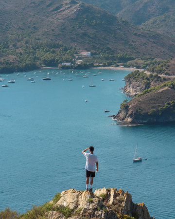 Young man standing on top of a cliff and looking at the seaの写真素材