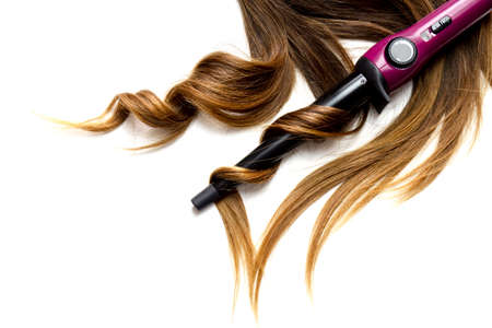 piece of brown curly shiny hair on white isolated background with curling waving ironの写真素材