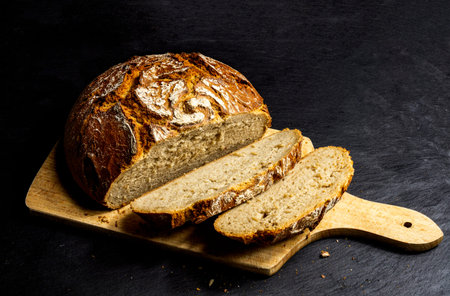 Sliced german farmers bread baurenbrot on a wooden board surface with black background