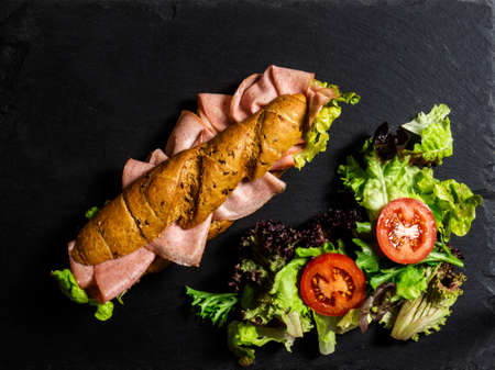 complete healthy deli sandwich kornspitz whole grain filled with meat slices and salad over dark background with copy spaceの写真素材