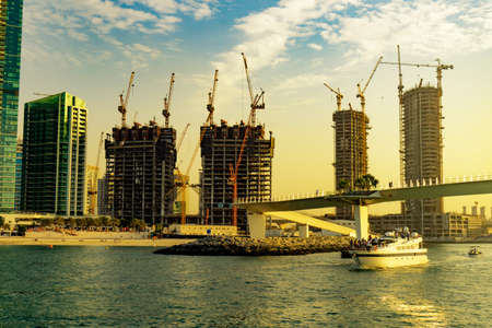 Dubai, UAE 11. 10. 2018 : Dubai contractions on the coast line with cranes everywere in sunset and a boat with touristsのeditorial素材