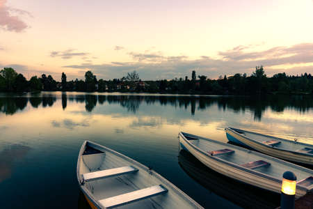 wooden boats on a calm lake called Csonakazo Lake in Szombathely Hungary at dusk after sunset next to the pierの写真素材