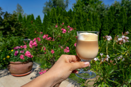 Drinking latte macchiato coffee at home on the terrace or garden with flowers in the background at...