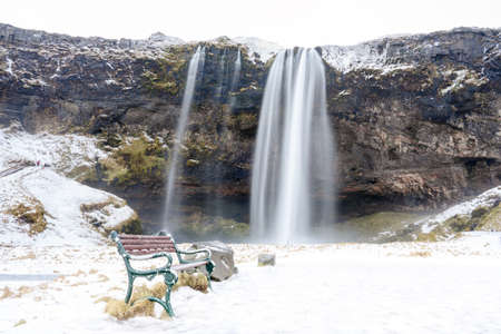 Seljalandsfoss waterfall in winter season with an benchの写真素材