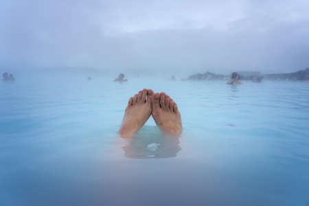 Feet of a woman bathing in the Blue Lagoon next to Reykjavik with people bathing in this natural hot springの写真素材