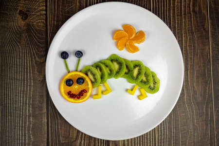 funny fruit worm on white plate healthy dessert for kids on wooden table .の写真素材