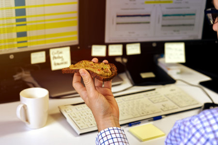 Busy business man eating healthy avocado toast breakfast in a hurry while working on computer