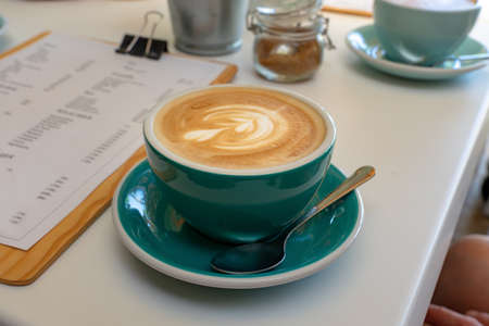 caffee latte macchiato cappuccino in blue turquoise mug in cafe house with milk foam art .の写真素材