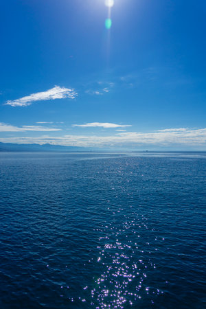 Calm blue sea with sparkling water under clear sky and distant coastal mountainsの写真素材