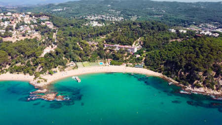 Beautiful aerial view of beach with ferry boat and resort in Cala Santa Cristina, Blanes, Costa Brava, Spainの写真素材