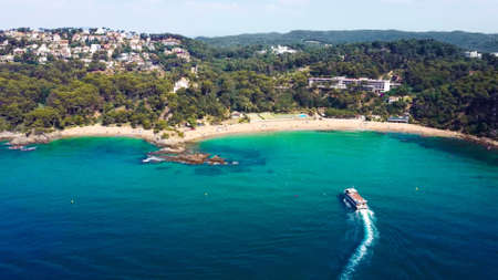 Beautiful aerial view of beach with ferry boat and resort in Cala Santa Cristina, Blanes, Costa Brava, Spainの写真素材
