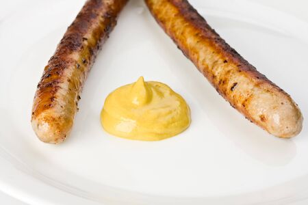 two grilled sausages on a plate with mustardの写真素材