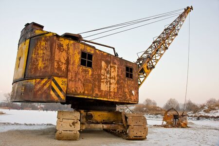 rusty old yellow excavator on a winter dayの写真素材
