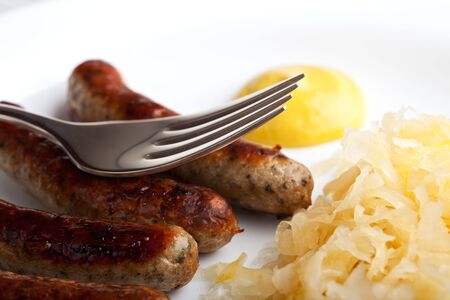 fried sausages,mustard and sauerkraut on a plate with a forkの写真素材
