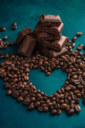 aromatic coffee beans with a heart and dark chocolate slices in the backgroundの写真素材