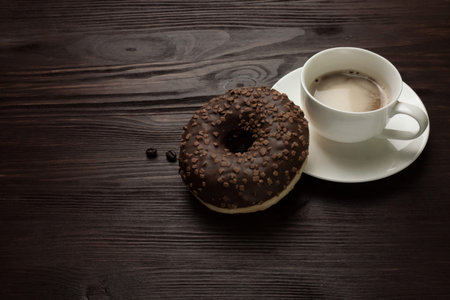 cup with coffee and chocolate donut on a dark wooden background side view