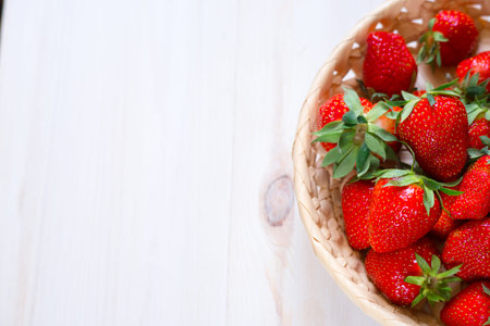 ripe red strawberries lie in a wicker basket on rustic white wooden background top view