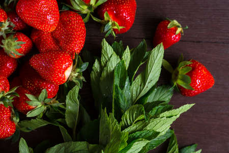 ripe red berries of strawberries and sprigs of fragrant mint lie on a dark wooden backgroundの写真素材