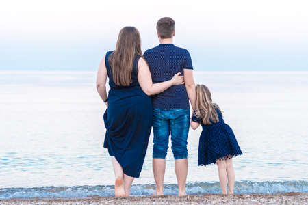 a young family dad mom and a little daughter are walking along the beach and watching the ocean, the sea. the concept of happy motherhoodの写真素材