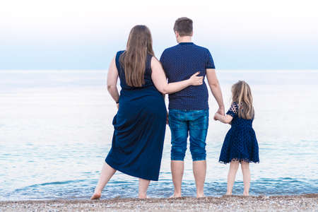 a young family dad mom and a little daughter are walking along the beach and watching the ocean, the sea. the concept of happy motherhoodの写真素材