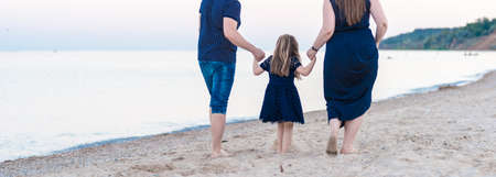a young family dad mom and a little daughter are walking along the beach and watching the ocean, the sea. the concept of happy motherhoodの写真素材