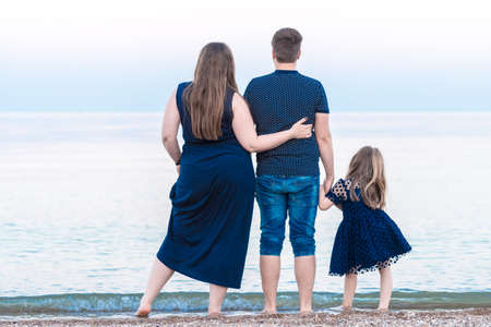 a young family dad mom and a little daughter are walking along the beach and watching the ocean, the sea. the concept of happy motherhoodの写真素材