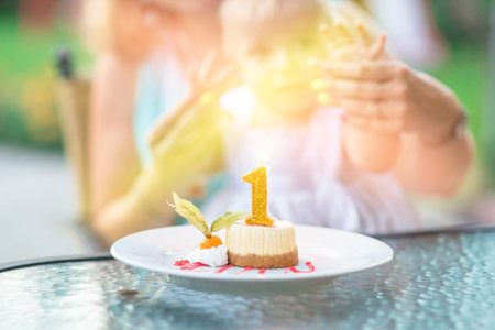 capkake with a candle in the form of a number one, in the background a blurred family mom and daughter in the rays of light . summer. happy birtdayの写真素材