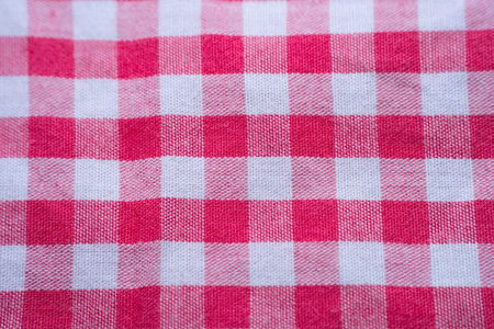 Top view of tied red ribbon bow on firebrick gingham pattern texture background, macro