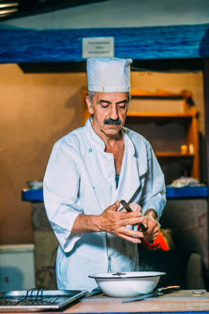 the cook in white uniform strips meat on a skewer on a background of the brazier with coalsの写真素材