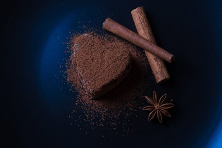 chocolate biscuit capkake in the form of heart sprinkled with cocoa powder lies on a dark background next to cinnamonの写真素材