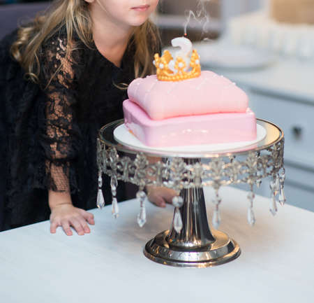 birthday little girl blowing a candle on a festive cakeの写真素材