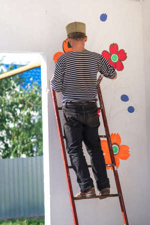 a man paints and paints paint a white wall with floral ornaments . summerの写真素材