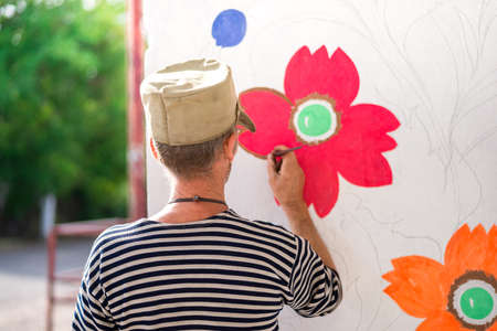 a man paints and paints paint a white wall with floral ornaments . summerの写真素材