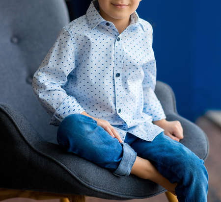 Cute boy resting in armchair with soft pillow at homeの写真素材