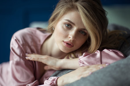 Portrait of a young beautiful blonde woman with wavy hair in a pink peignoir with a deep cut. Text spaceの写真素材