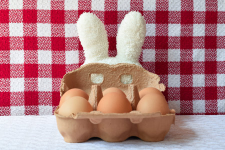 White toweling bunny ears with a carboard mask and eggs. White and red checkered background and...