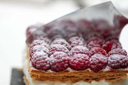 Spatula cutting a fresh raspberries cake with powdered sugar.Delicious cream pastry
