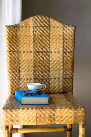 Blue book, white cup and eyeglasses on a chair.の写真素材