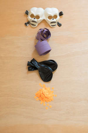 Halloween party elements. Plastic skull glasses, purple streamer, black balloons and orange confetti on a wooden surface.の写真素材