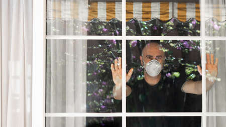 Adult man wtih a mask protection looking through the window.の写真素材