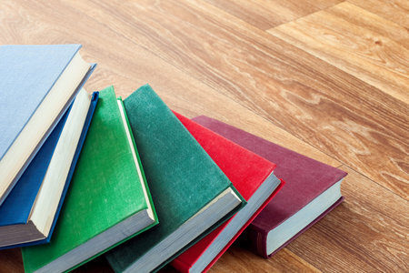 Books in a firm cover lie one on one on a surface of a wooden table.