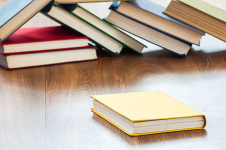 Books lie on a wooden table, the sharp book in the foreground and a lot of the scattered unsharp...