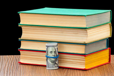 The pile of books lies on the wooden table glad with them the twisted dollars in a tubule.の写真素材