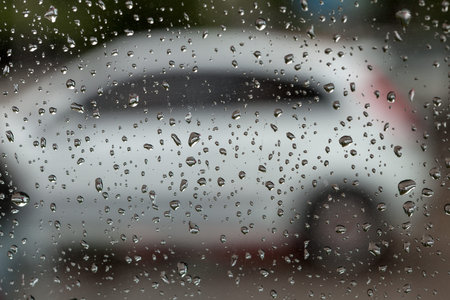 The rain drop on glass, behind glass is stood by the white car.