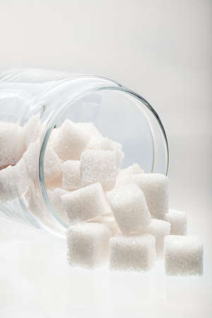 White lump sugar in a glass jar on a white background, sweet sugar in the ware lying on one side nobody.の写真素材